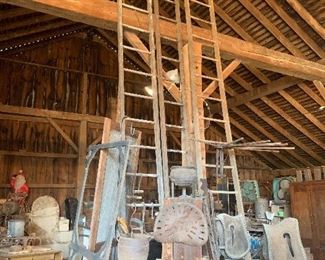 3 TALL antique wood ladders, old wall mount wood drying rack, old screen door frames, antique box with advertising on the side, old tractor seat, assorted vintage hand saws, a few 5' 2 man wood saw blades (one with partial wood box)