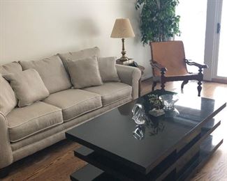 New couch with 3-seat detached cushions,  mid-century modern black coffee table, plantation chair, and side table with brass lamp.  Also Steuben bowl and objects of art