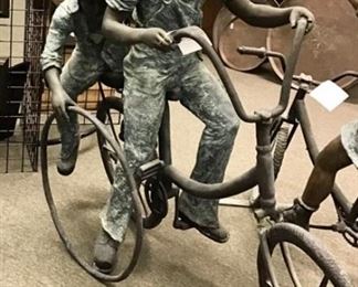 Joyous bronze sculpture modeled after 1900s period boys riding a bike and rolling a wheel. Solid bronze. 8 ft long x 59” tall x 24” wide