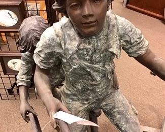 Joyous bronze sculpture modeled after 1900s period boys riding a bike and rolling a wheel. Solid bronze. 8 ft long x 59” tall x 24” wide