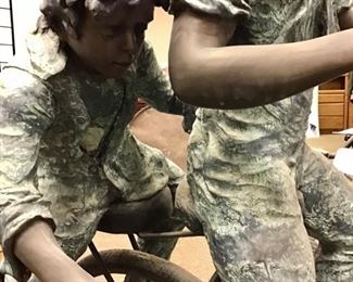 Joyous bronze sculpture modeled after 1900s period boys riding a bike and rolling a wheel. Solid bronze. 8 ft long x 59” tall x 24” wide