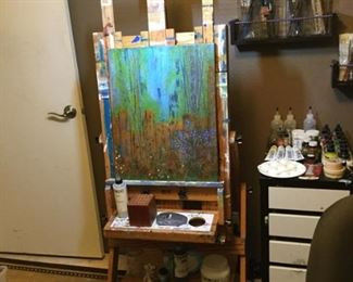 Artist easel in wood and wall shelves for paint supplies