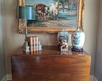 Vintage drop-leaf cherry table, Stiffel table lamp, matched pair of Asian porcelain urns on wooden bases, leather-bound books and large original oil on canvas - cows doing what cows do: dare to stare. 