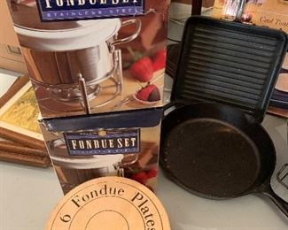 $50- lot of kitchen items; two fondue pots with fondue plates, one Lodge cast iron pan, a  large commercial frying pan, Presto griddle, All Clad griddle and a roaster. 