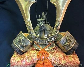 Full Size “Japanese Warrior” Helmet $300
My father acquired this piece when he traveled to Japan. It is a heavy “Japanese Warrior” Helmet for display. It is metal, accented with brass and sits on an decorative pillow. The helmet measures 16” wide x 9 ½” deep x 14” high (highest point). The sides of the helmet are accented with tigers, the “blades” of the helmet are accented with dragons and there is a metal dragon that sits atop the helmet. Please note that I believe the tail of the dragon may have a couple of broken “spikes” as they feel rough. It is not visible from the front view, but this was taken into account with the pricing. When the helmet sits atop the pillow, it measures 16” wide x 13” deep x 17” high (highest point).