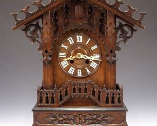 An early 20th century German Black Forest mantle cuckoo clock by Gordian Hettich & Sohn, Furtwangen.  Good quality Brass 8-day time and strike movement with Cuckoo and Gong strike.  Walnut case with scalloped pediment crest, pierced dial crest, picket fence detail on a stepped molded base cut out bracket feet.  French retailer's label from Marseille inside case.  Original finish with Ebonized detail, older repairs, lacks one finial on fence, running but strike needs adjustment.  21 3/4" high.  ESTIMATE $1,000-2,000