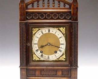 A late 19th century Winterhalder & Hofmeier bracket clock, retailed by Elkington & Co., London (England).  8-day time and strike movement with Brass dial and Silvered chapter ring, Roman numerals and cast spandrels, quarter hour "Bim-Bam" striking on two gongs.   Walnut case with arched gallery top, above a Gothic style frieze and a single door, flanked by carved columns on a base with turned feet.  Old finish with slight wear, minor damage, running when cataloged.   14 1/2" high overall.  ESTIMATE $300-400