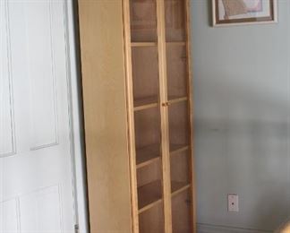 Blonde pine, glass doored book case	
5 adjustable shelves. This is a large, fragile piece.
Measurements 31"x12"x79"