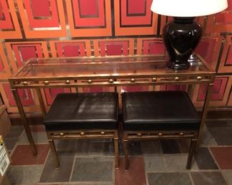 Item 55: Glass top metal table with two bench seats $165 Glass is free of chips or cracks. Seats are upholstered in black vinyl with piping. One stool has four impressions in the vinyl as shown. Good condition.
