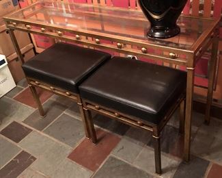 Item 55: Glass top metal table with two bench seats $165 Glass is free of chips or cracks. Seats are upholstered in black vinyl with piping. One stool has four impressions in the vinyl as shown. Good condition.