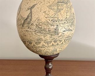 Item 198: Scrimshaw Decorated Ostrich Egg w/ Whaling  Scene seated on brass stand.  The whaling scene depicts ships, whales, mythological figures, etc.: $775