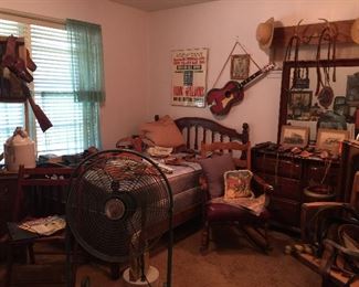 Looking into the Western Room! vintage full size bed, rocking chair, oak office chair, dressing table with mirror and lots of storage. Hanging rack with antlers, lots of leather gun holsters on the bed, belts, art work