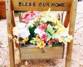 $10.  BLESS OUR HOME WOODEN PLANT STAND WITH FAKE PLANTS IN IT.