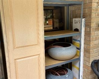 Shelving, water hoses in decorative urns, tall cabinet.