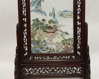 1174	HAND PAINTED ASIAN PORCELAIN PLAQUE IN AN ORNATE CARVED STAND, OVERALL DIMENSIONS ARE 16 3/4 IN W, 26 3/4 IN H 
