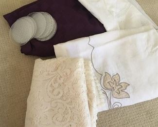Item #93:  Lot of assorted tablecloths.  Apprx. 66" rd/lace is apprx. 84"x54"; beige w/flower is apprx. 60"x72"/purple is 84"rd.  Coasters included.  $15