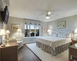 King bed with Tuft and Needle mattress, wicker furniture, large rug, chair and lamps.