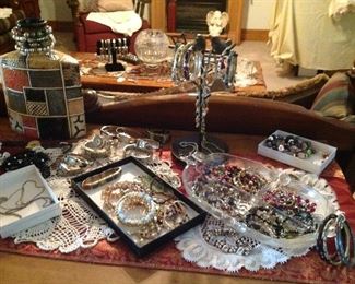 Entertainment center topped with table runner, doilies, decorative bottle and lots of Jewlery.