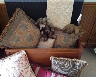 Chest full of decorative pillows and mink look teddy bear and dog