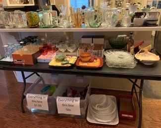 Den: Bar is covered in decanters, pitchers, and more.  Table full of sets of drinking glasses, chip and dip plates, stacks of cake  and deviled egg plates.  On the floor, bargain boxes, and large white serving dishes.
