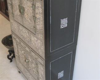 A Korean stacking chest in black lacquer inlaid with mother of pearl featuring birds and animals in  a landscape setting.