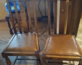 2 of 4 antique wooden chairs with leather seats.