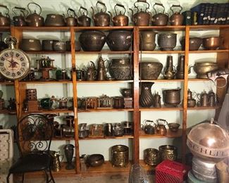 Garage wall with Budweiser advertising clock, vintage copper and brass tea kettles of all shapes and sizes, intricately carved pots and pipe holders.