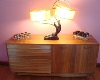 Dining Area:  A walnut Mid-Century Modern "American of Martinsville" sideboard has three drawers with louvered fronts (see next photo for close-up) on the left as well as three more drawers and two shelves behind the two flat panel cabinet doors on the right (as shown in an upcoming photo).  It measures 60" wide x 18-l/2" deep x 30" tall and matches the nearby display credenza.  The lamp is flanked by two sets of Dorothy Thorpe-style glasses.