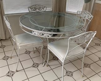 Wrought Iron & Glass Kitchen Table Set with Four Chairs. Chairs and table has a floral motif; glass is 49" in diameter, table is 29" tall.