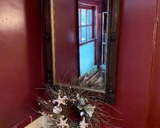 Behind the commode is a large piece of mercury glass a seashell wreath and an antique Victorian mirrior 