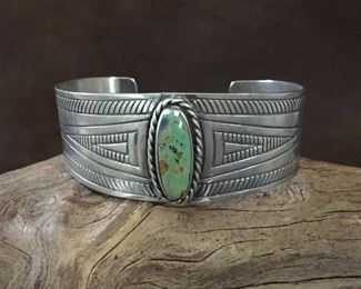 #12...Signed Native American made sterling silver and turquoise cuff bracelet. Stamped with cool tribal design and features a beautiful green turquoise cabochon. Total circ. 6 7/8" (5 7/8 " inner circ. with 1" gap). Width tapers from 1" at center front to 5/8" in back. Signed with pictorial mark (looks like a lower case f), circle c and 88. Stamped STERLING. Slightly flexible. $340