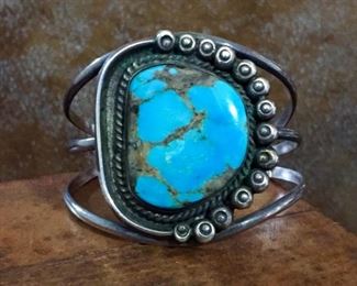 #20...Native American made old pawn sterling silver and turquoise cuff bracelet. The center medallion has a D-shaped turquoise cabochon framed in rope-style silver wire on surrounded on the right side with fourteen stamped silver raindrops. Center medallion is 1 5/8" x 1 7/8". Total circ. 6 1/2" (5 1/8" inner circ. with 1 3/8 " gap). $600
