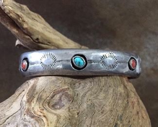 #38...Native American made sterling silver cuff bracelet with one turquoise and two coral cabochons in shadowbox settings. Cuff has eyelash stamps all around and a pair of snake eye stamps on each side. Total circ. 7 1/8" (5 5/8" inner circ. with 1 1/2" gap). 1/2" wide all around. Slightly flexible. $300