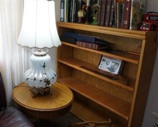 bookshelf,  lamp, one of two oval end tables, books, picture albums, mirror