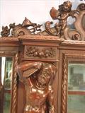 110 - 1911 China Cabinet by Oriel Cabinet Co. that features massively carved mascarons, Norman soldiers, atlantes and caryatid figures as well as griffins in full relief (part of the "Norman Suite"), 94in. tall, 66.5in. wide, 19in. deep (atlantes figure, 2)