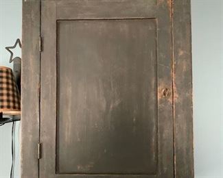 Chamfered and paneled door hanging cupboard in dark green dry surface paint.