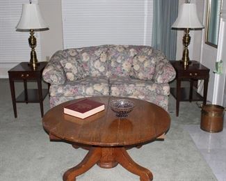 Antique Empire Style Oak Round Pedestal Table.  Table has been mortified from a dinning table to a cocktail/coffee table.(42”D x 18”H). Vintage Hepplewhite Mahogany End Tables with single drawer (24”H x 16”W x 23.5”D).  Also shown Hamilton House Tapestry Floral Upholstered Sofa/Loveseat and a pair of Heavy Brass Table Lamps