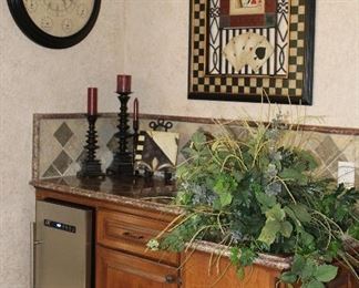 View of wet bar displaying; Silk Green Arrangement, Fleu De Lis Decor Tile, Westgate Candle Stands and Bombay Co 24” World Time Wall Clock