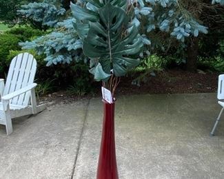 Lot 1456.  $45.00. Lovely red glass vase with banana palm fronds. Vase is 38"tall and12"W 		