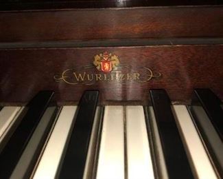 Detail of an upright Wurlitzer piano. It has straight lines and dark wood, nice looking.