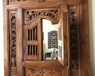Wooden carved wall decor with mirror hidden behind doors, above credenza in dining room.