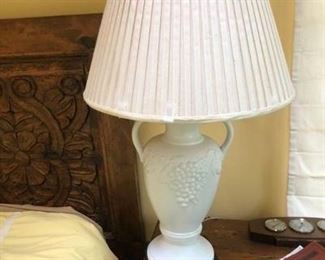 A white lamp on a night stand in master bedroom.