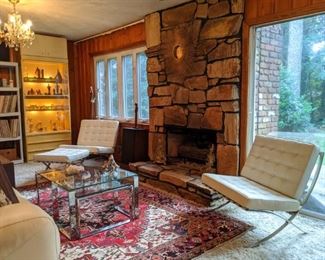 2-piece glass/chrome coffee table, hand woven Persian Heriz rug, pair of white leather Barcelona-inspired chairs, one with matching ottoman, large, brass brutalist sunburst wall art above the fireplace, lighted lacquered curio cabinet, one of a pair of 6-light crystal chandeliers and a peek at the several hundred vinyl albums.