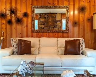 Fresh white leather couch, with brass brutalist sea urchins, daintily creeping up the walls.