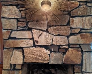 Close-up of the brass brutalist sunburst wall art and vintage brass French andirons.