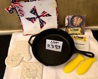 Lot 2383. $20.00. Lodge Preseasoned Cast Iron Skillet (looks brand new), with instructions and 2 silicone handles. 1 flag hot pad, 2 ceramic hot pads.