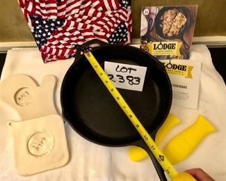 Lot 2383. $20.00. Lodge Preseasoned Cast Iron Skillet (looks brand new), with instructions and 2 silicone handles. 1 flag hot pad, 2 ceramic hot pads.