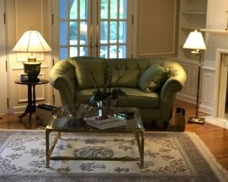 Large square glass coffee table with brass legs, small green sofa, rosewood side table, medium rug