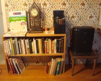 Bedroom #1:  Office supplies, a metal wire clock, and books are to the left of a paper shredder and tile top table.