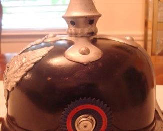 Near Cashier: This is a side view of the Prussian guard helmet which shows a dark blue and red cockade [or roundel] which  represented the colors of a specific German state, e.g., Oldenburg.  The other side of he helmet has a black/white/red cockade which represented the Imperial national colors.  